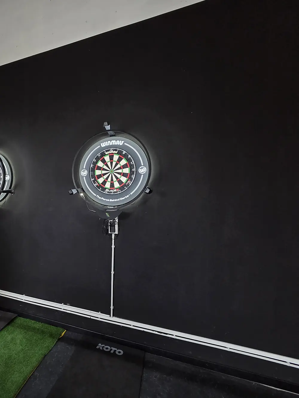 Two lit electronic dartboards on a black wall